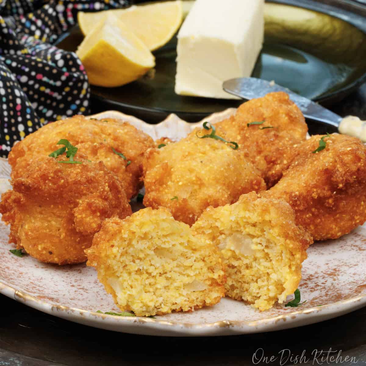a small batch of hush puppies on a plate next to butter.