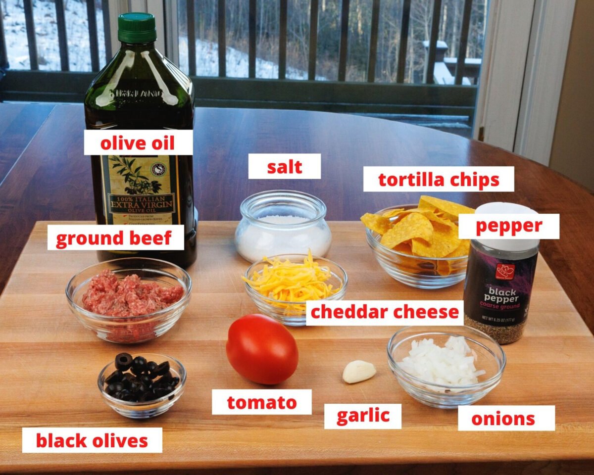 ingredients needed to make beef nachos on a wooden cutting board.