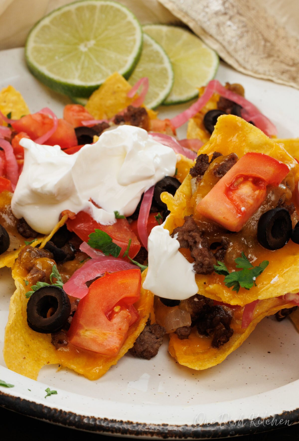nachos with ground beef and sour cream on a white plate.