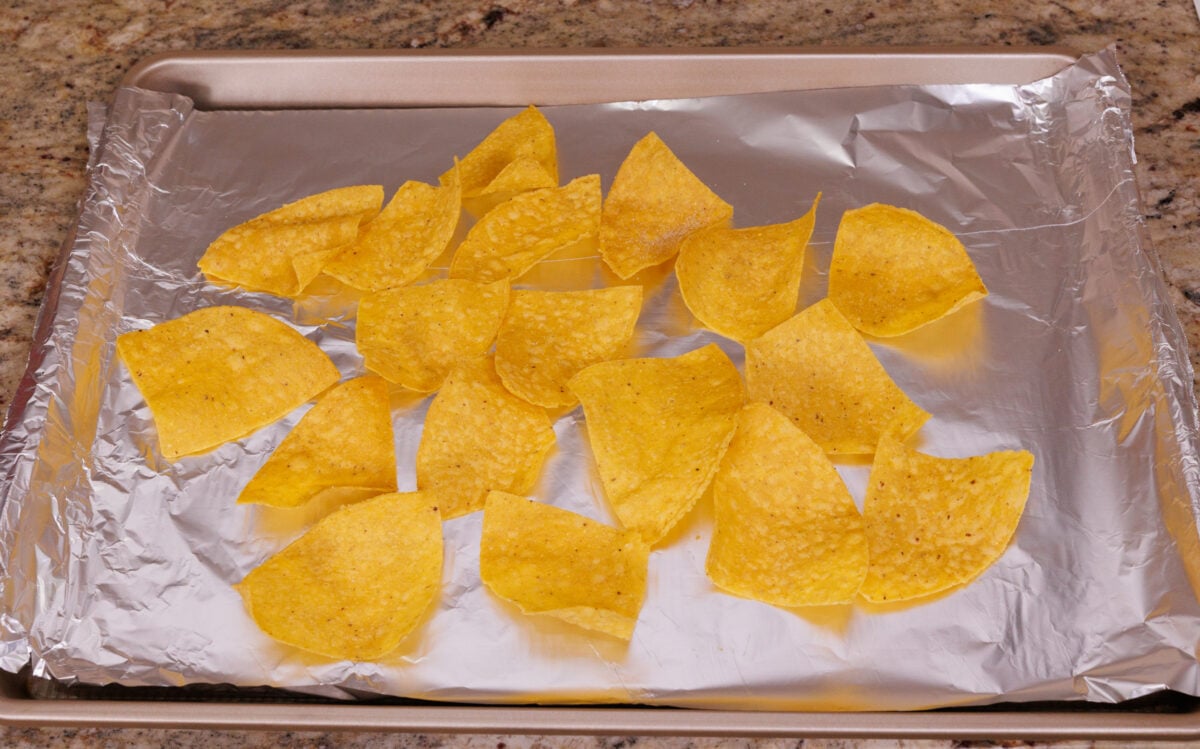 tortilla chips spread out on a foil lined baking sheet.