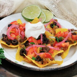 a plate of beef nachos with slices of lime on the edge of the plate