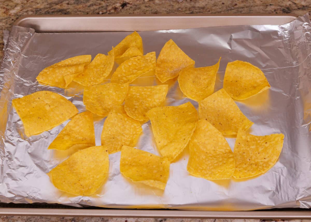tortilla chips spread out on a foil lined baking sheet.