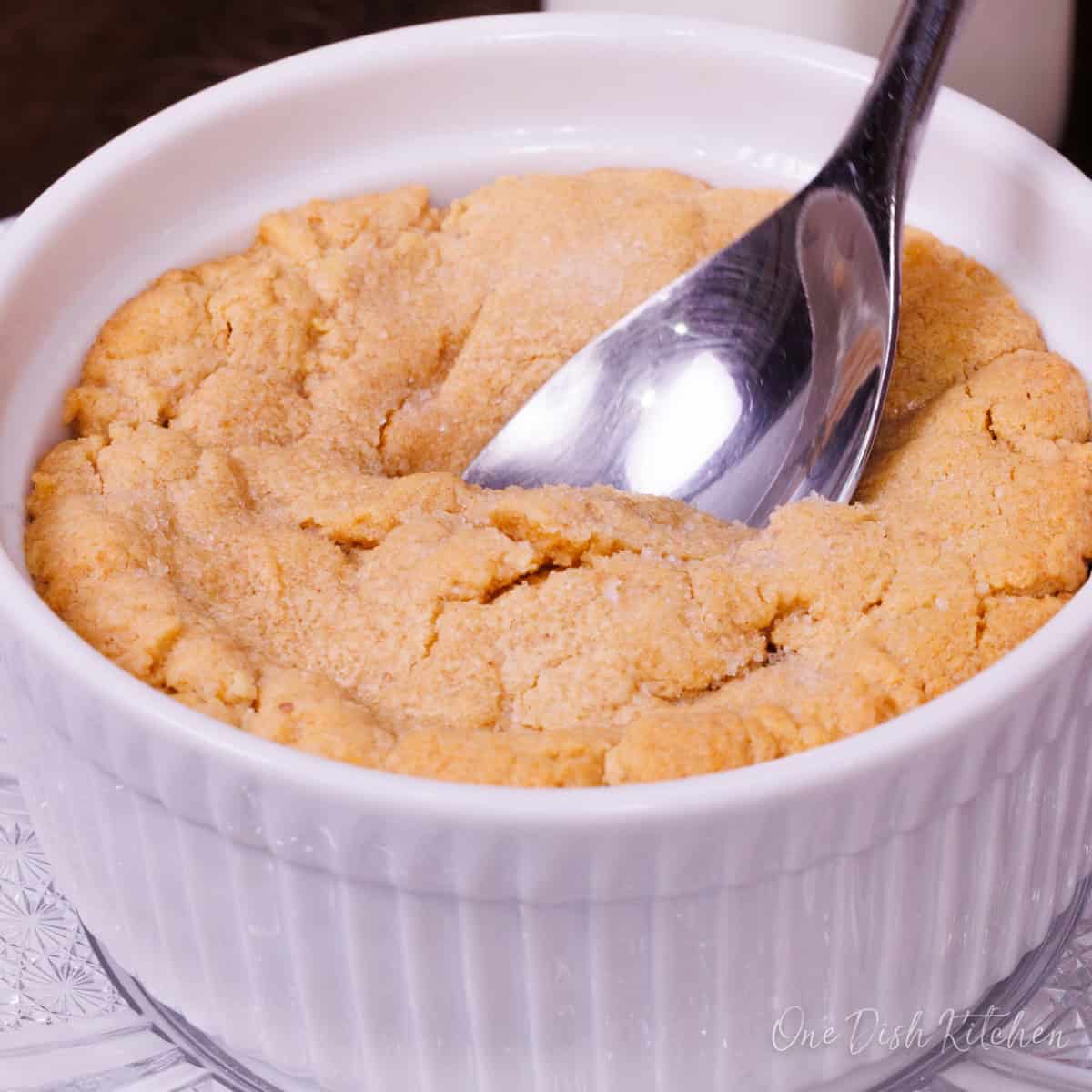 a single serve peanut butter cookie in a deep dish ramekin with a spoon on the top.