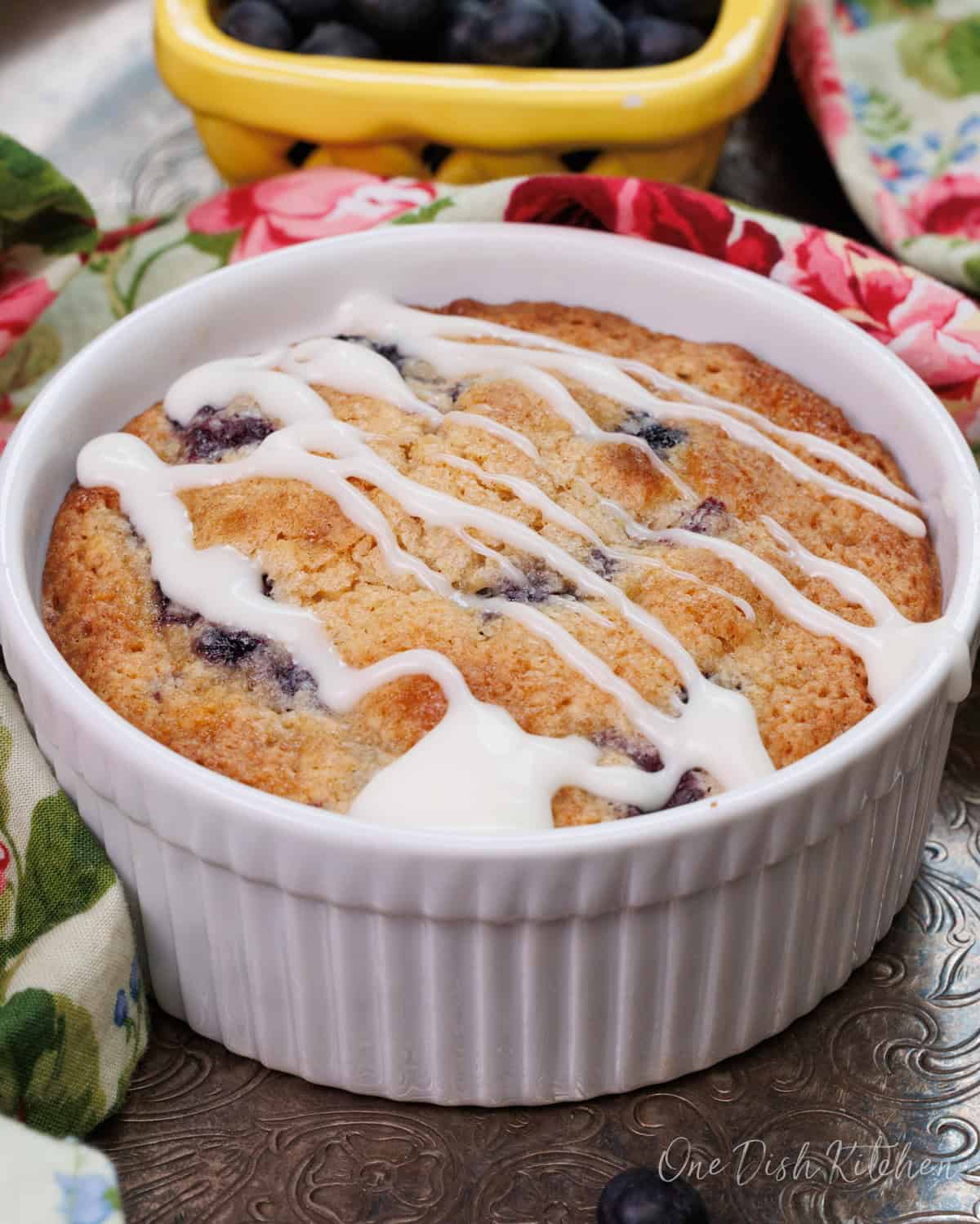 a small blueberry coffee cake in a white ramekin on a silver tray.