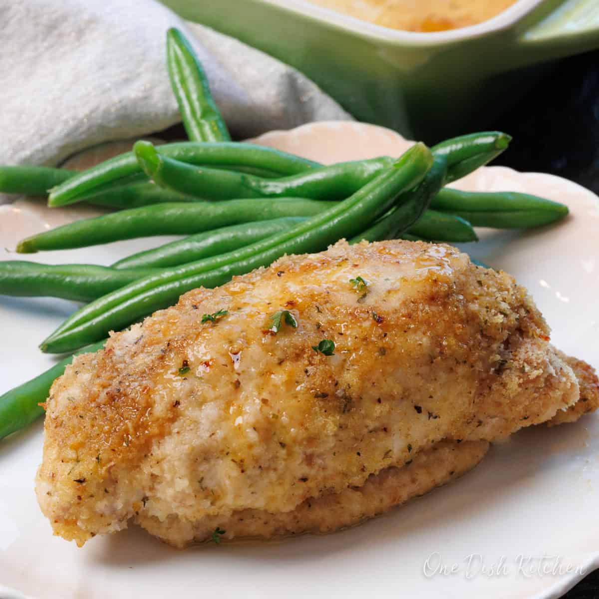 chicken cordon bleu on a white plate next to fresh cooked green beans.