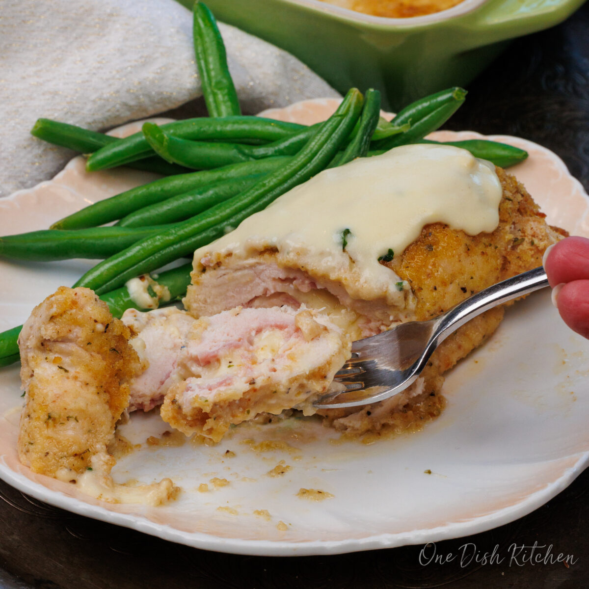 a fork with a piece of chicken cordon bleu on it next to the remaining piece of chicken.