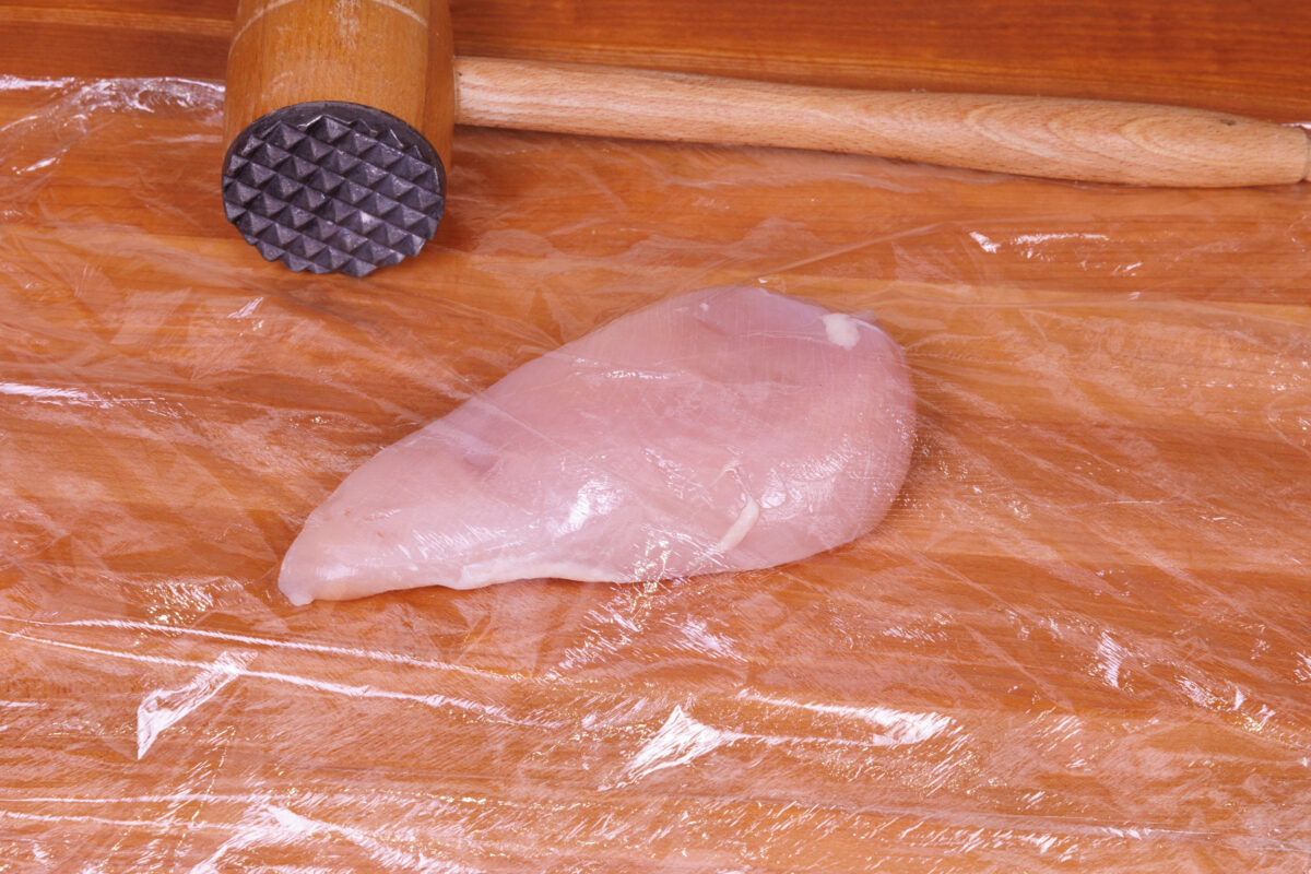 one raw chicken breast on a wooden cutting board.