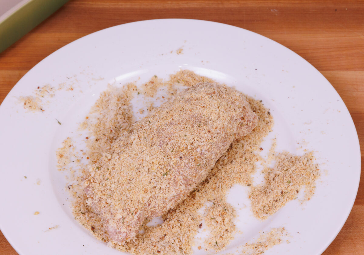 chicken rolled up and dipped in breadcrumbs on a white plate.