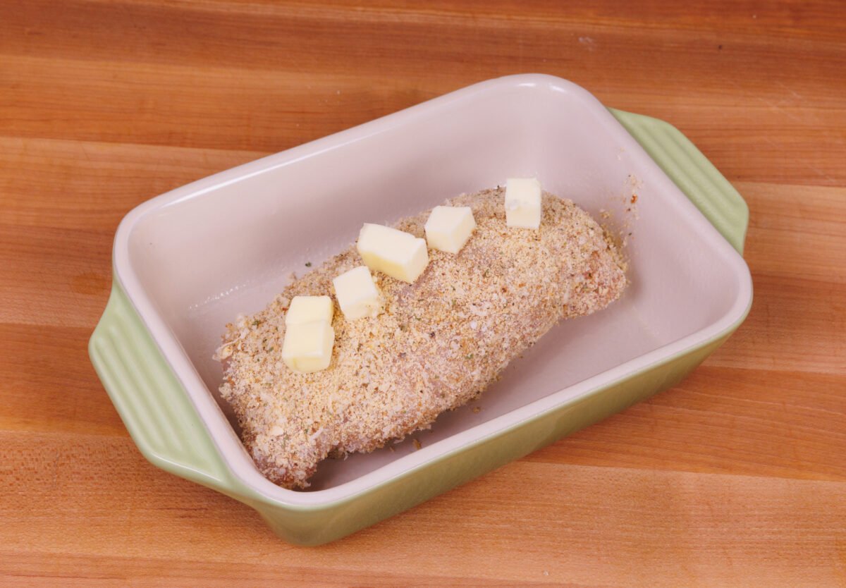 unbaked chicken cordon bleu in a small baking dish topped with butter.