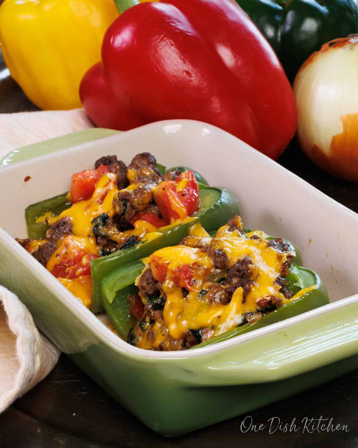 stuffed bell peppers in a baking dish next to a red, yellow, and green pepper on a silver tray.