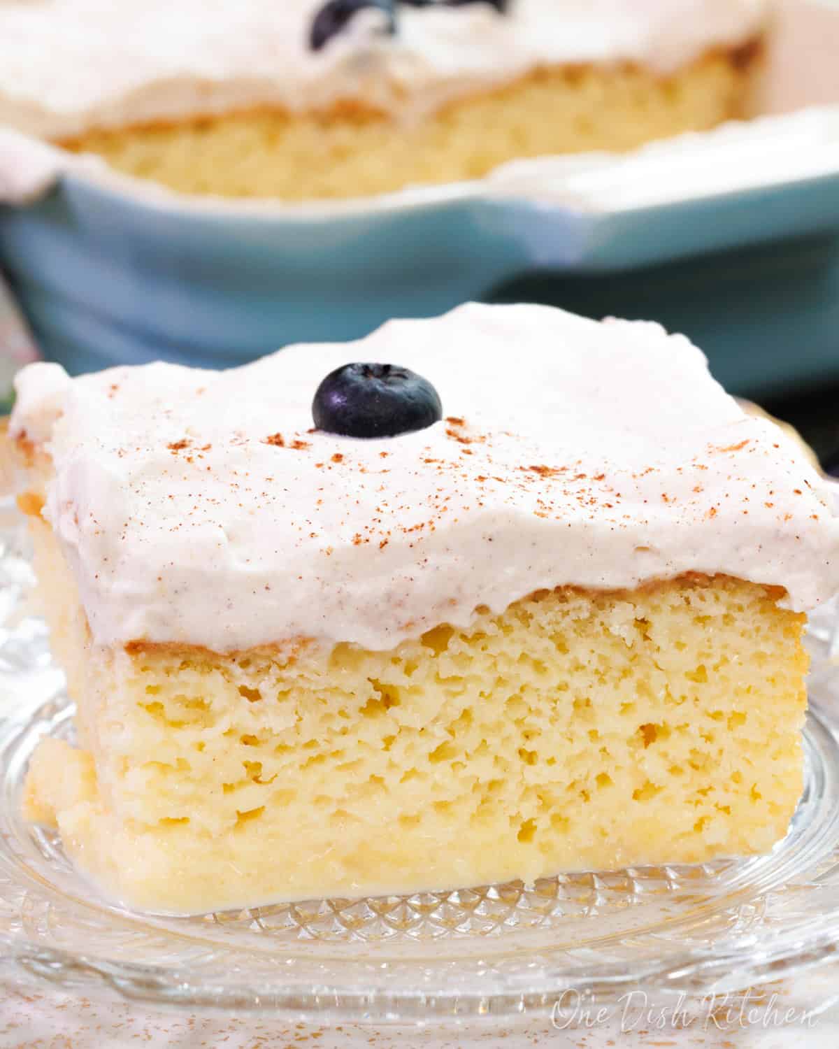 a slice of tres leches cake topped with a blueberry on a white plate.