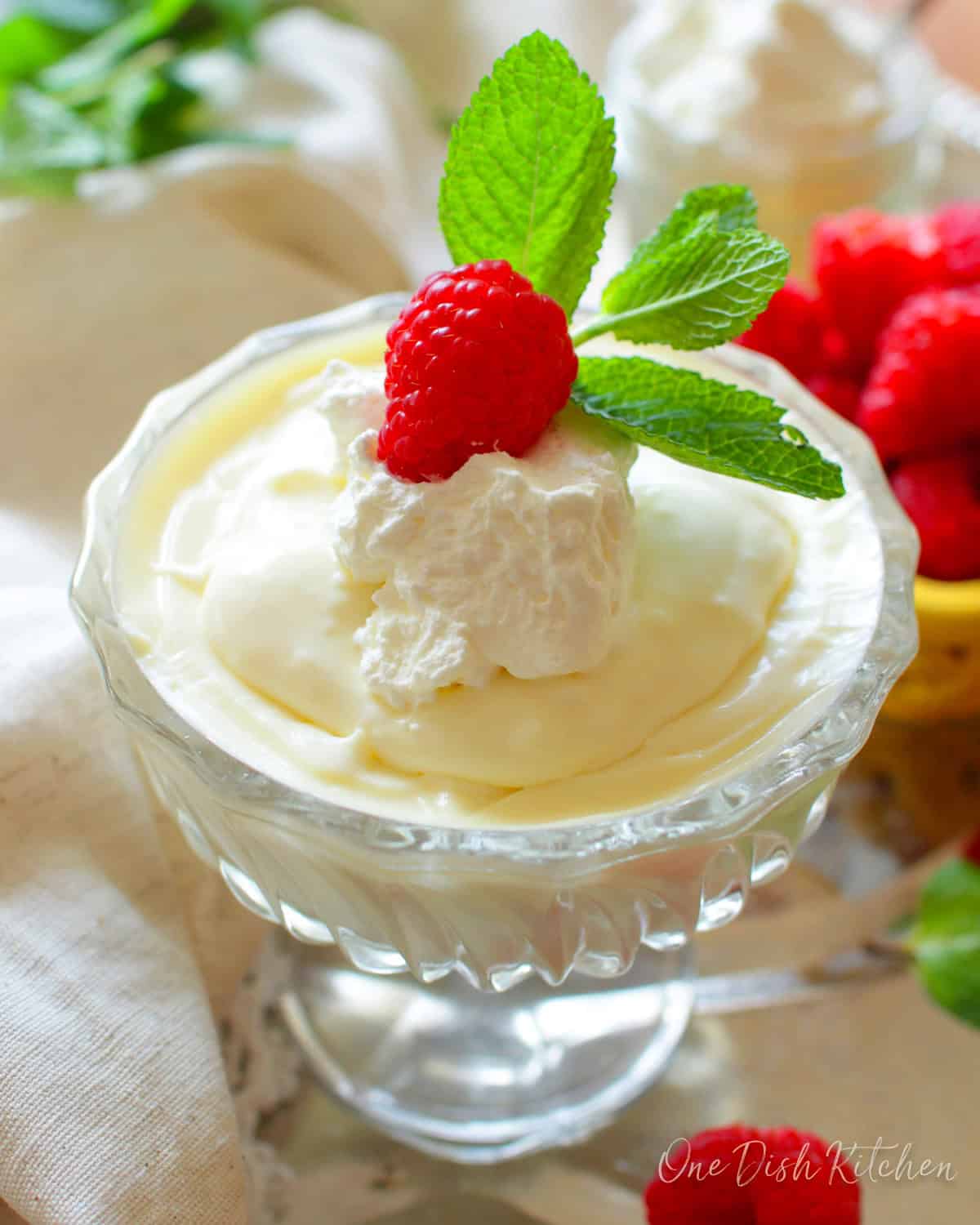 homemade vanilla pudding in a dessert bowl topped with whipped cream, berries, and fresh mint.