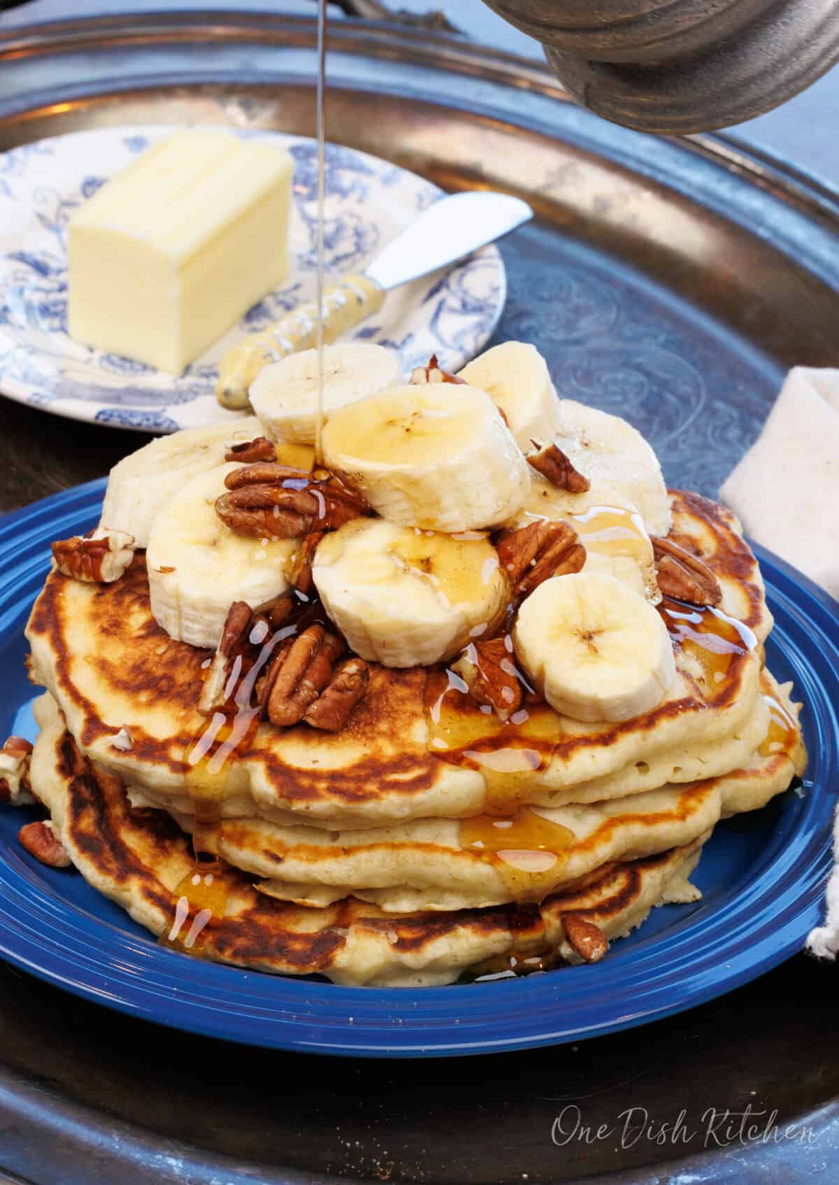 three banana pancakes on a blue plate topped with slices of bananas and pecans.