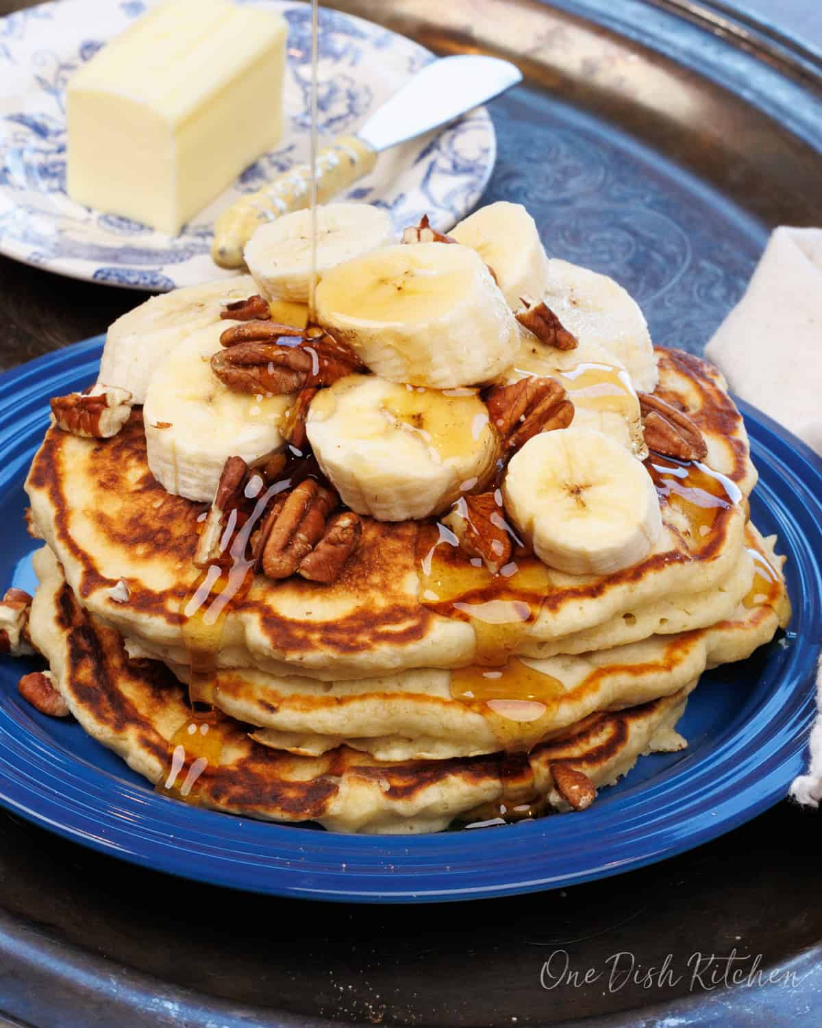 three banana pancakes on a blue plate topped with slices of bananas and pecans.