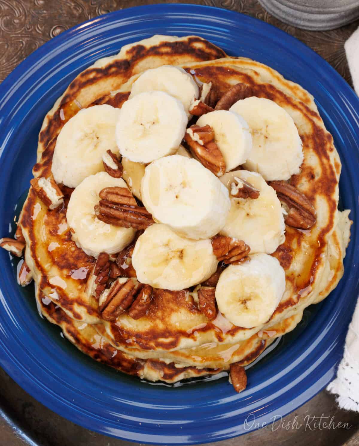 a overhead view of three banana pancakes topped with pecans on a silver tray.