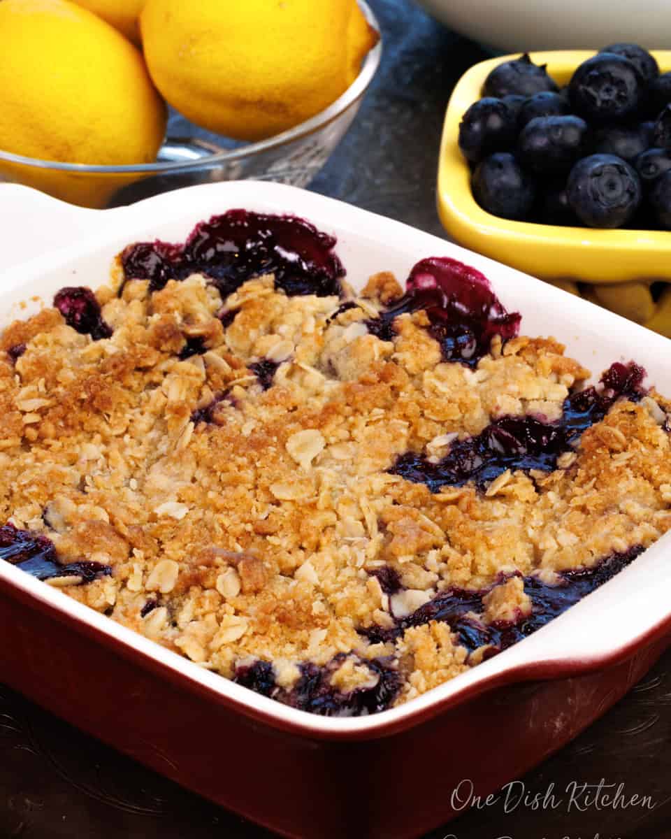 a blueberry crisp in a rectangular baking dish next to a bowl of blueberries.
