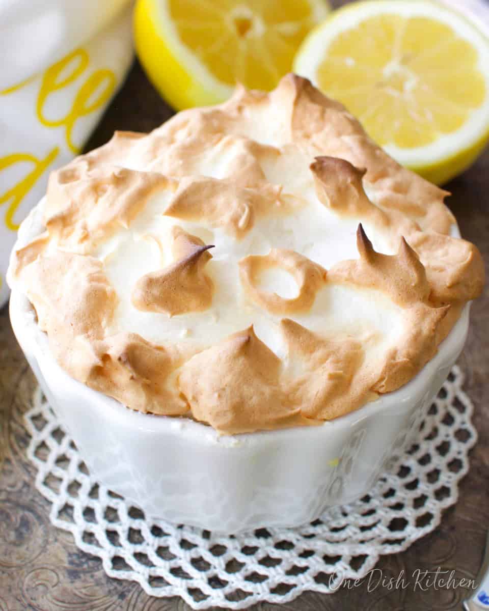 a small lemon meringue pie next to fresh lemons on a silver tray.