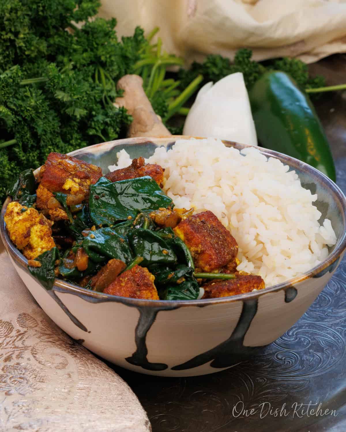a small bowl of saag paneer with rice on a silver tray next to onions and parsley.