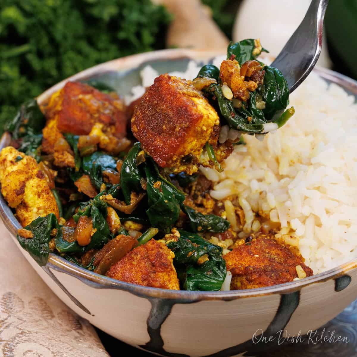 a fork filled with paneer and spinach over the bowl of saag paneer.
