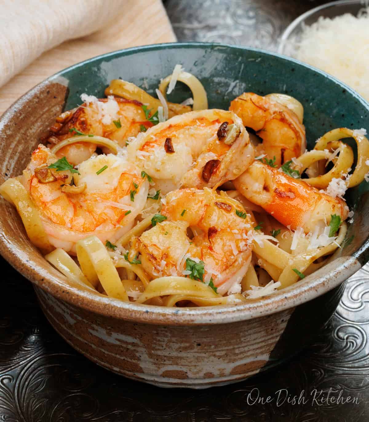 a bowl of shrimp fettuccine on a silver tray next to a fresh block of parmesan cheese.