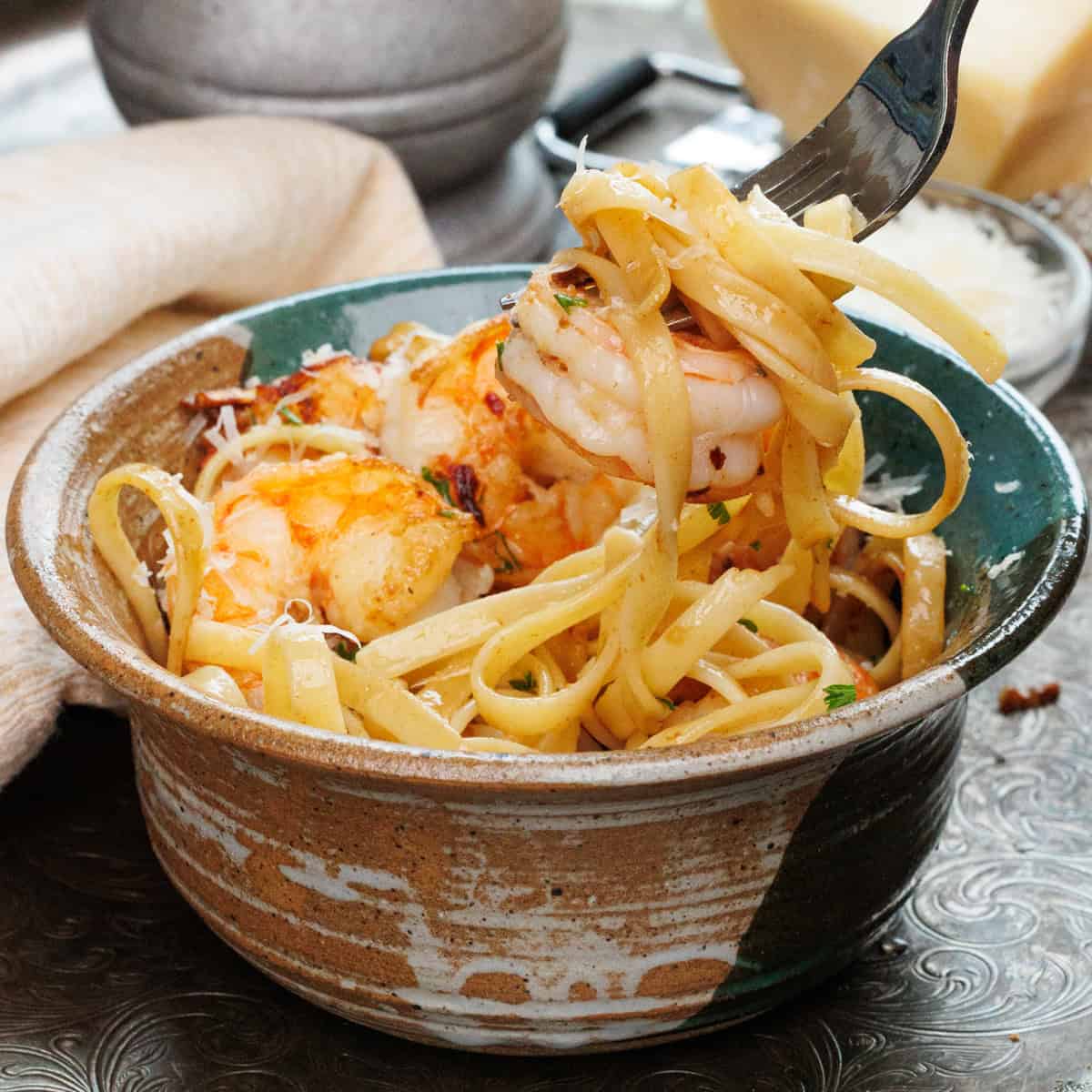 shrimp and fettuccine on a fork over a big bowl of pasta.
