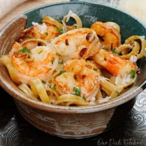 a bowl of shrimp fettuccine on a silver tray next to a fresh block of parmesan cheese.