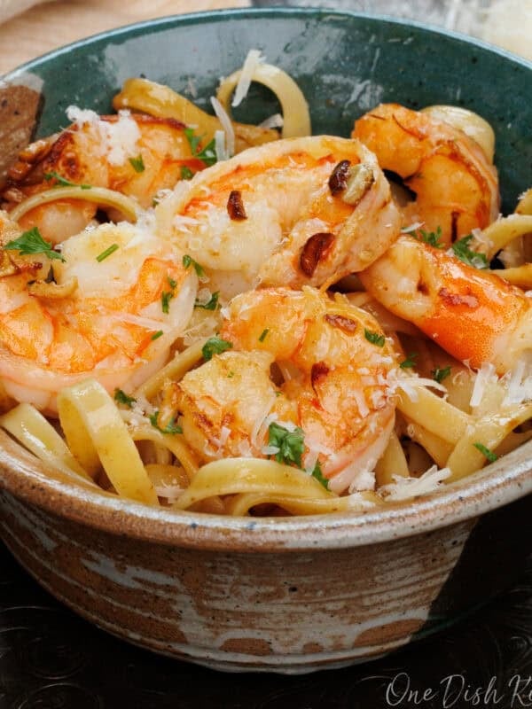 a bowl of shrimp fettuccine on a silver tray next to a fresh block of parmesan cheese.