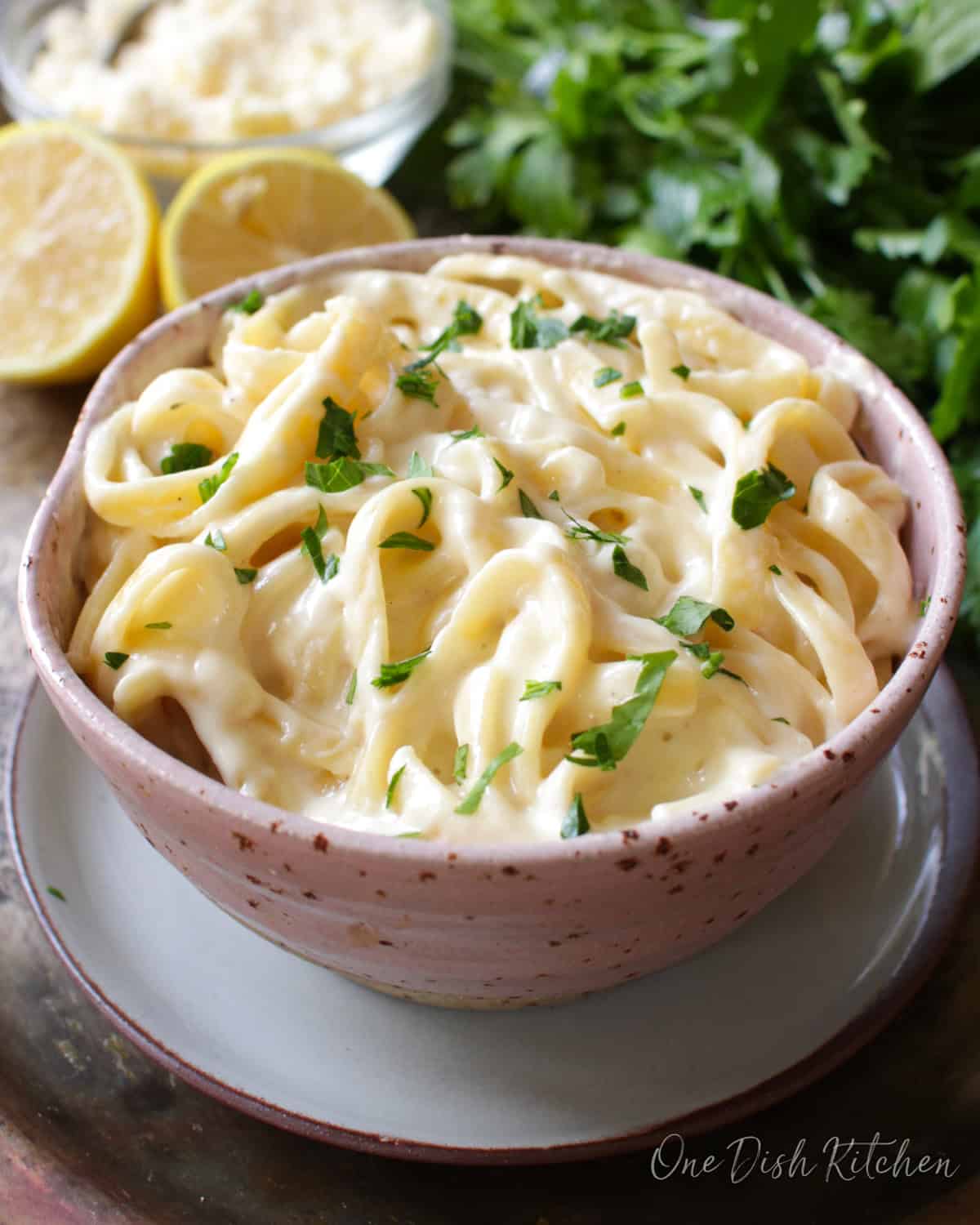 a pink bowl filled with fettuccine alfredo next to sliced lemons.