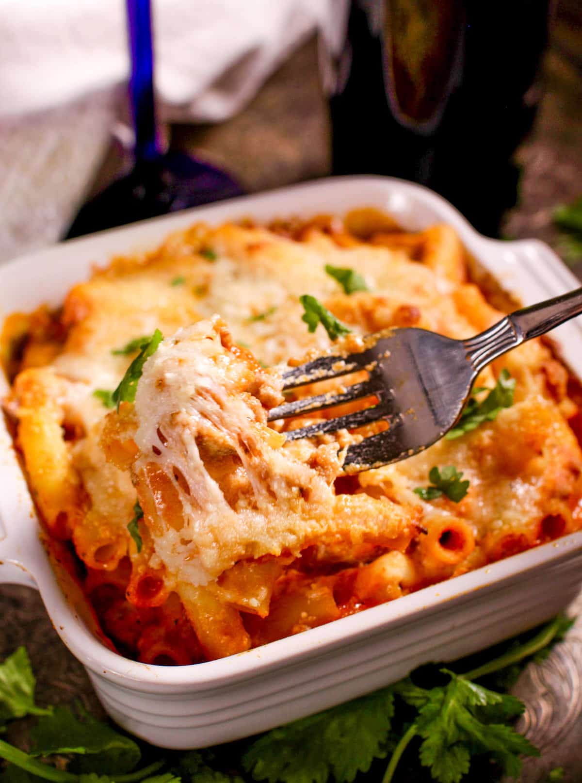 baked ziti in a small white baking dish next to a glass of red wine