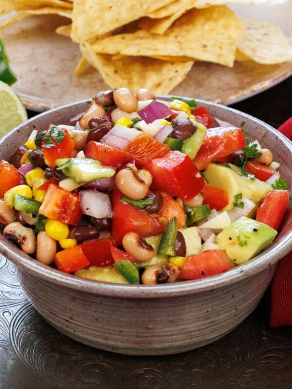 a bowl of cowboy caviar on a silver tray next to a plate of tortilla chips and slices of limes