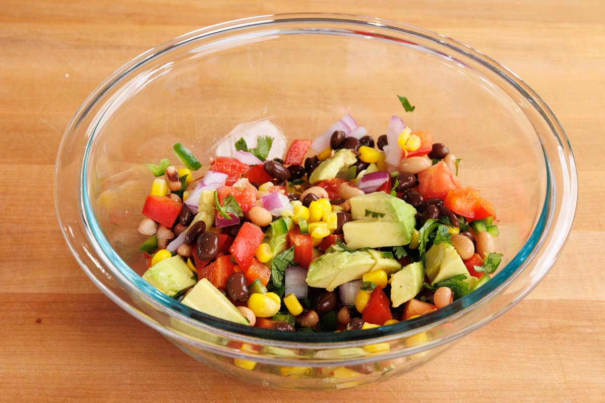 a bowl filled with corn, peppers, beans, avocados, and cilantro