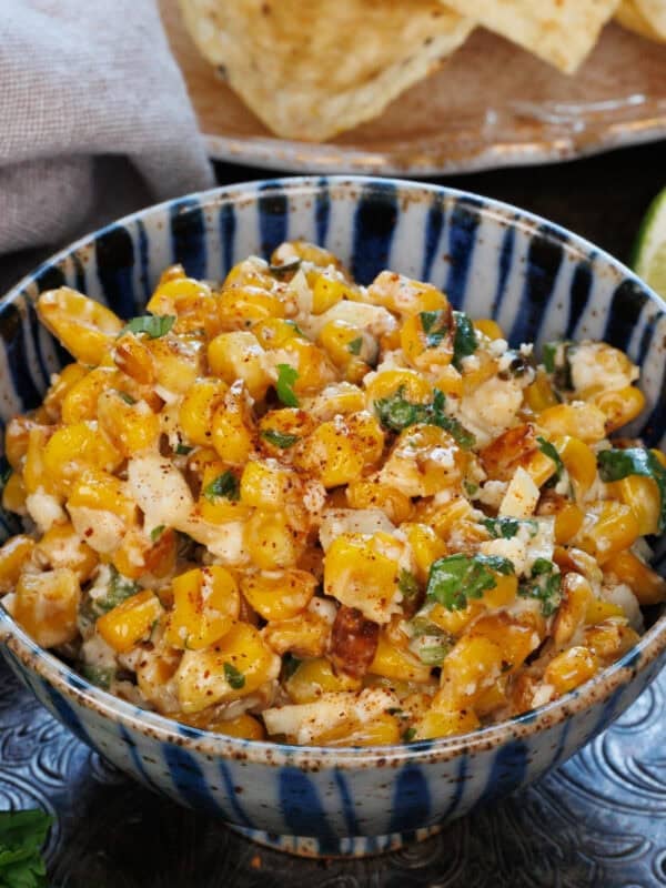 a small bowl of mexican street corn dip next to a bowl of tortilla chips.