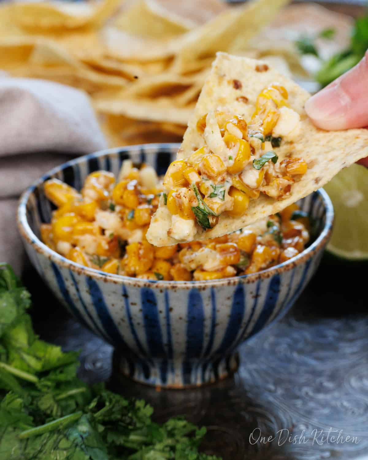 a bowl of esquites next to a plate of tortilla chips.