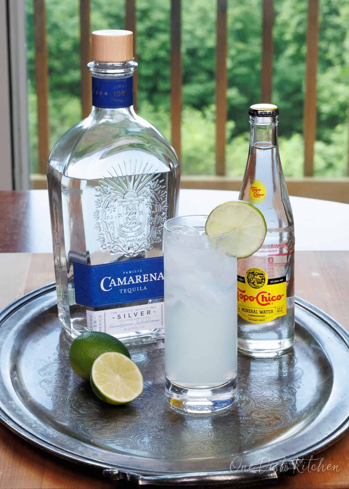 ranch water next to a bottle of tequila, limes, and sparkling water.
