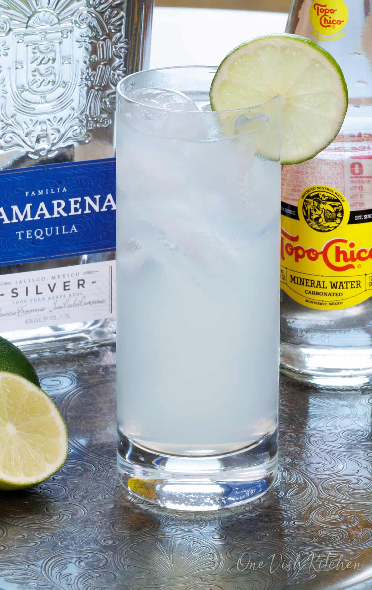 a glass of ranch water on a silver tray next to a half of a lime, topo chico, and tequila.