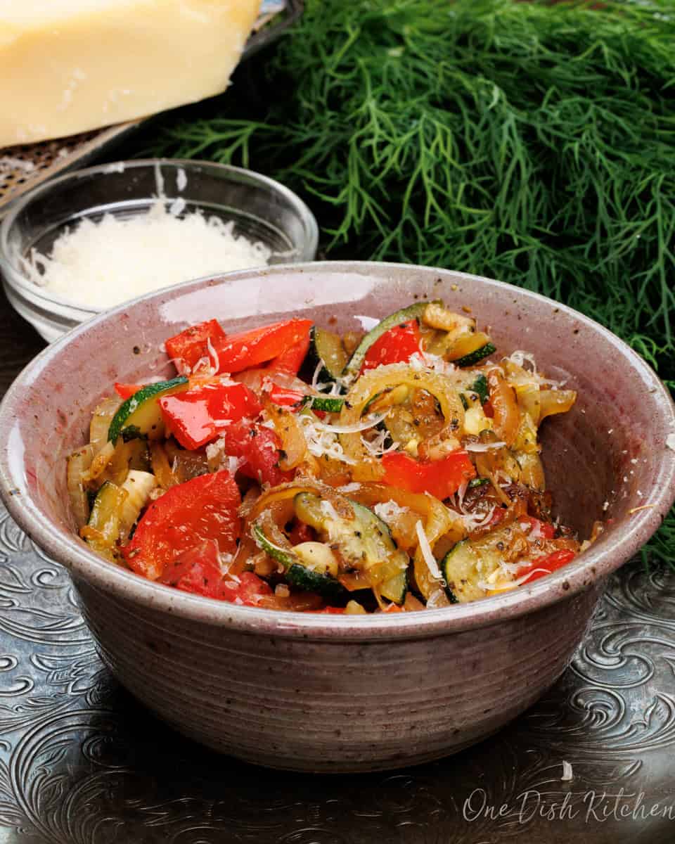 a bowl of ratatouille next to a bowl of fresh grated Parmesan cheese.