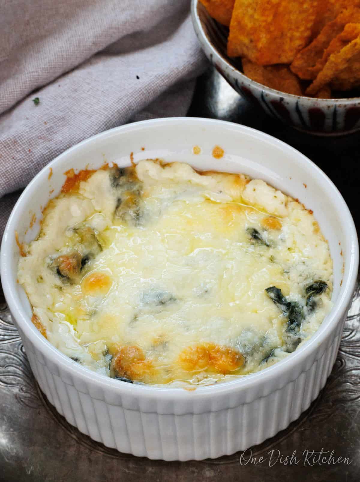 a small hot spinach dip in a bowl next to a plate of chips.