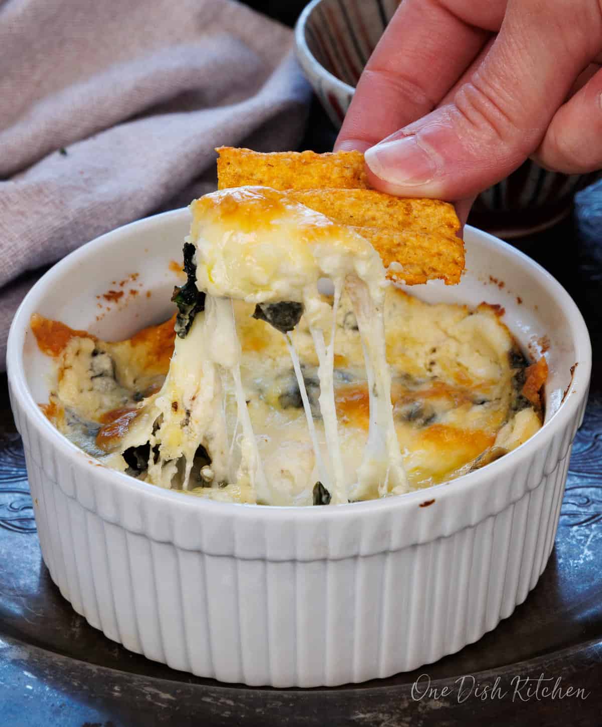 a chip scooping out spinach dip from a bowl.