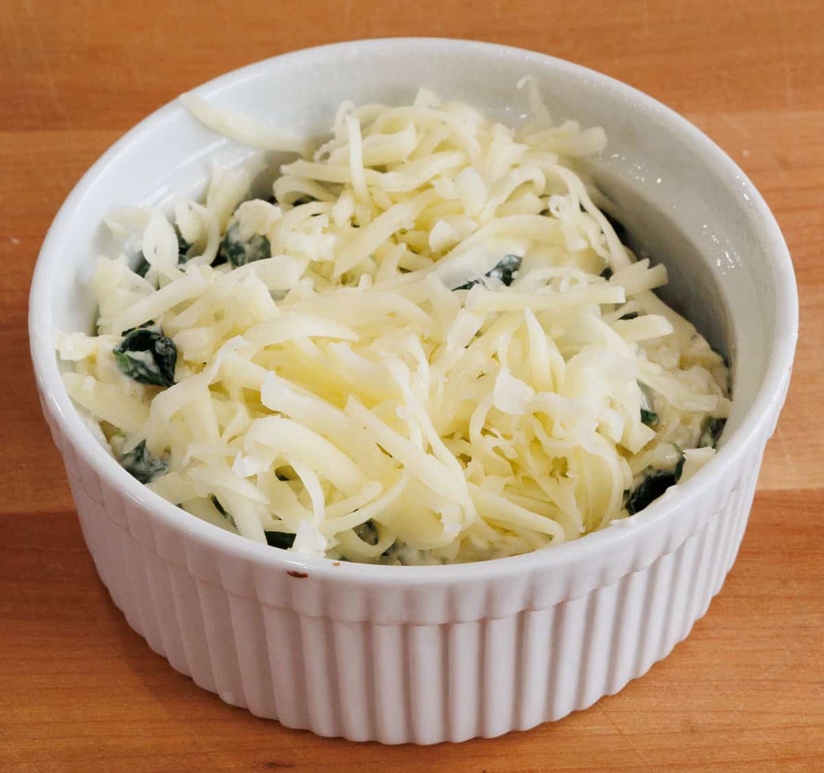 unbaked spinach in a ramekin on a wooden table.