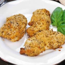 three baked chicken strips on a plate next to fresh basil.