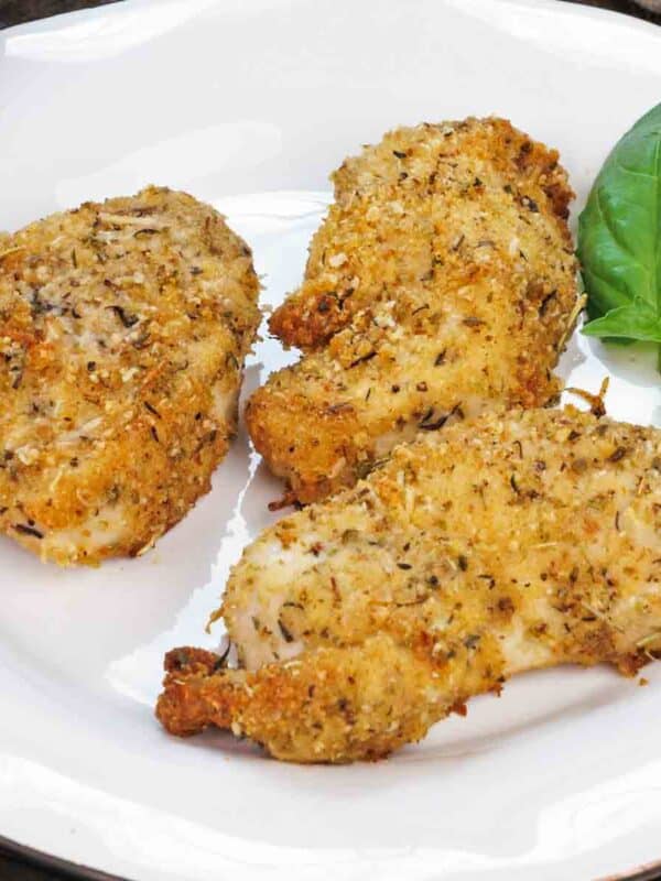 three baked chicken strips on a plate next to fresh basil.