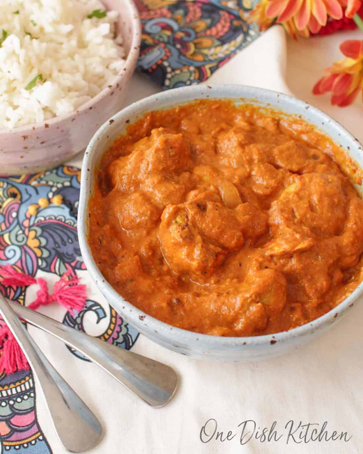 a blue bowl filled with butter chicken next to a bowl of white rice.