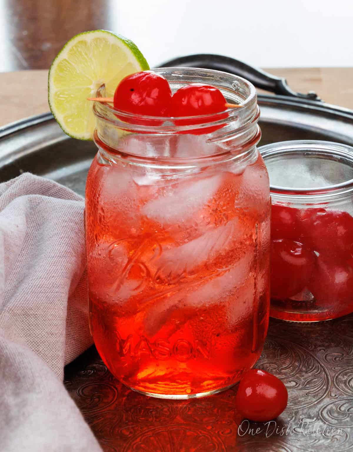 a dirty Shirley cocktail on a silver tray next to a bowl of maraschino cherries