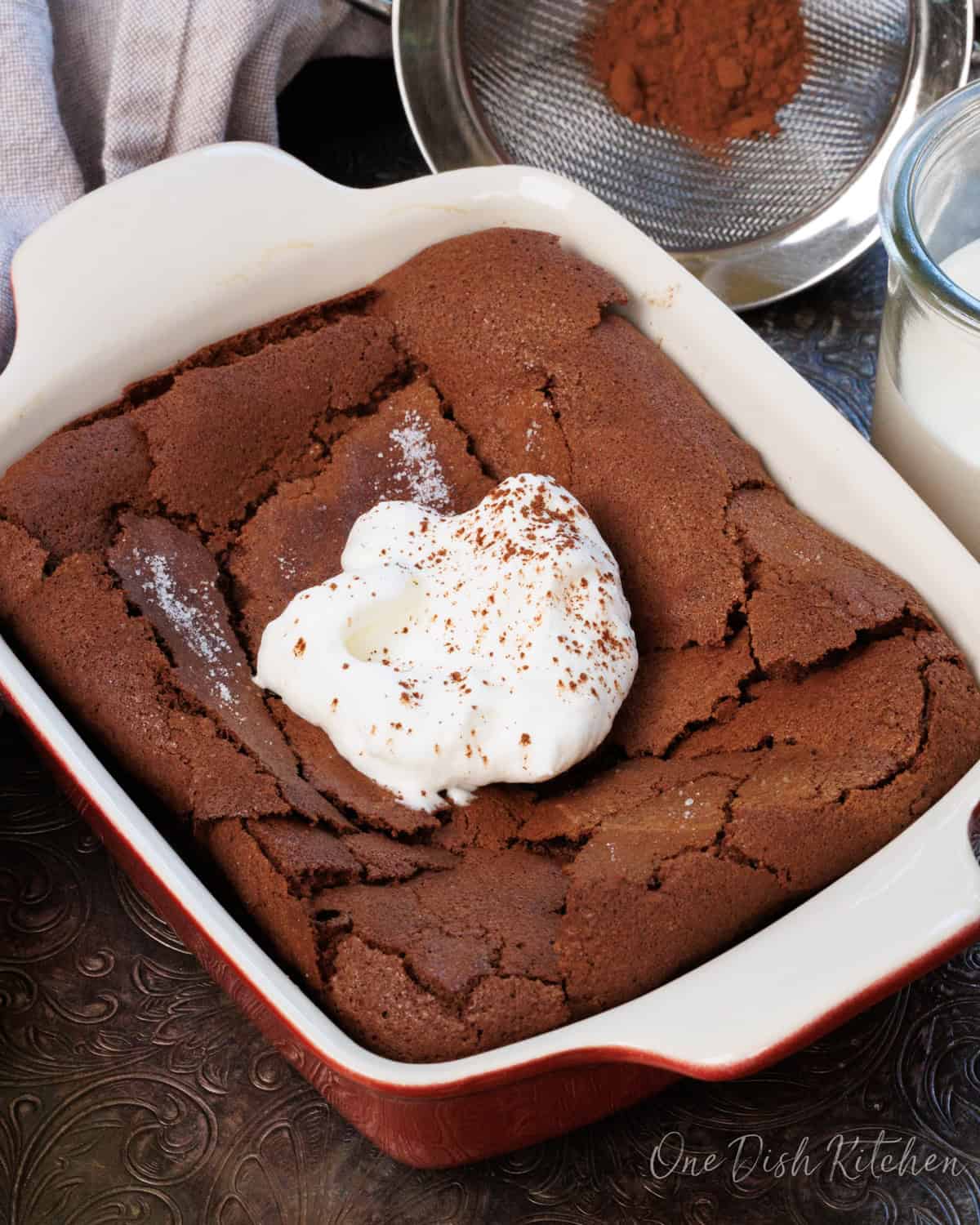 a chocolate flourless cake topped with whipped cream and a dusting of cocoa powder.