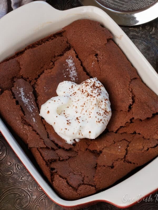 a chocolate flourless cake topped with whipped cream and a dusting of cocoa powder.