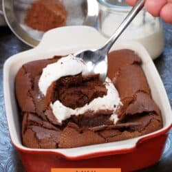 a small flourless chocolate cake in a red baking dish with a spoon on the side.