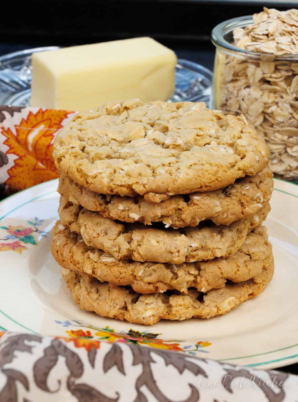 a stack of oatmeal cookies on a black tray next to butter and a jar of oats.