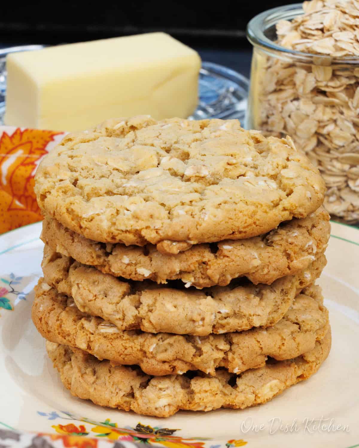 a stack of oatmeal cookies on a black tray next to butter and a jar of oats.