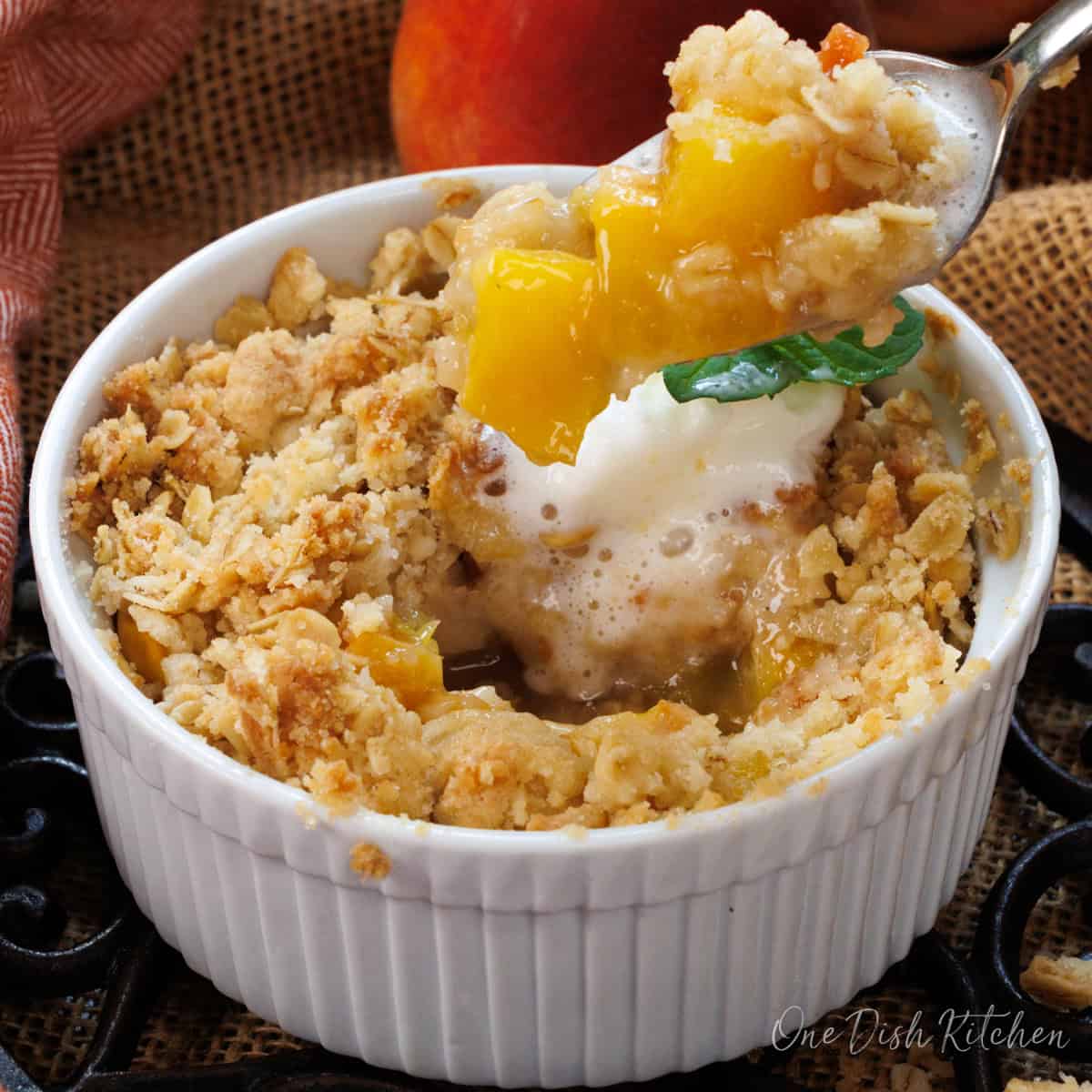 a spoonful of peach crisp next to the bowl.