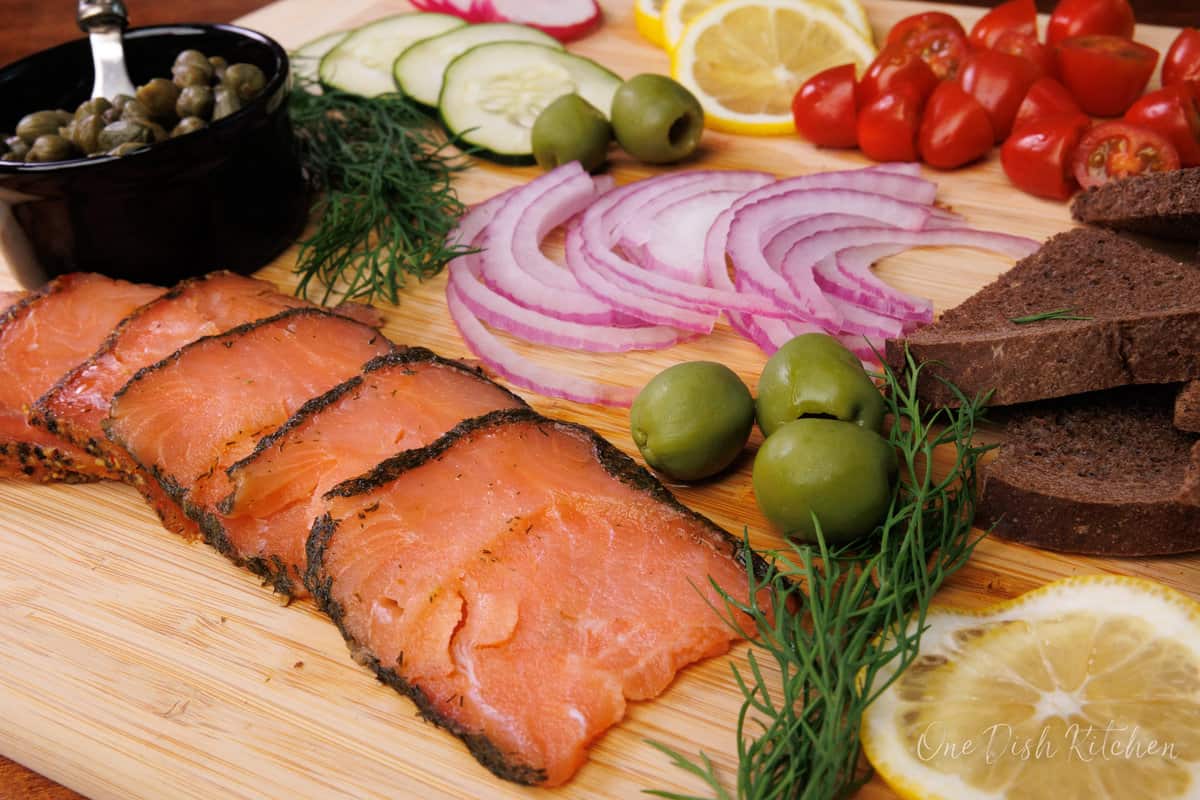 slices of smoked salmon on a wooden platter next to dill sprigs.